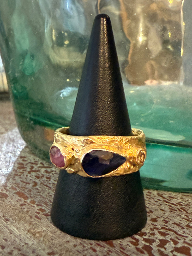 Gold ring with purple stones on a black cone stand against a textured surface.