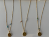 Three gold necklaces with circular pendants on a white background