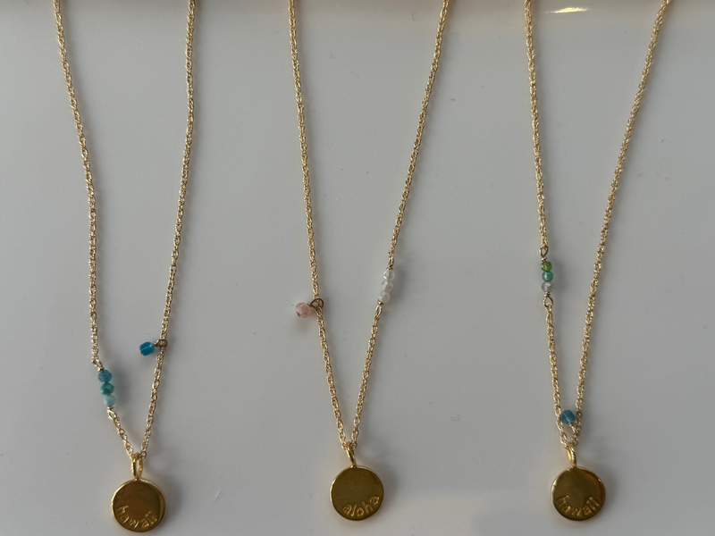 Three gold necklaces with circular pendants on a white background