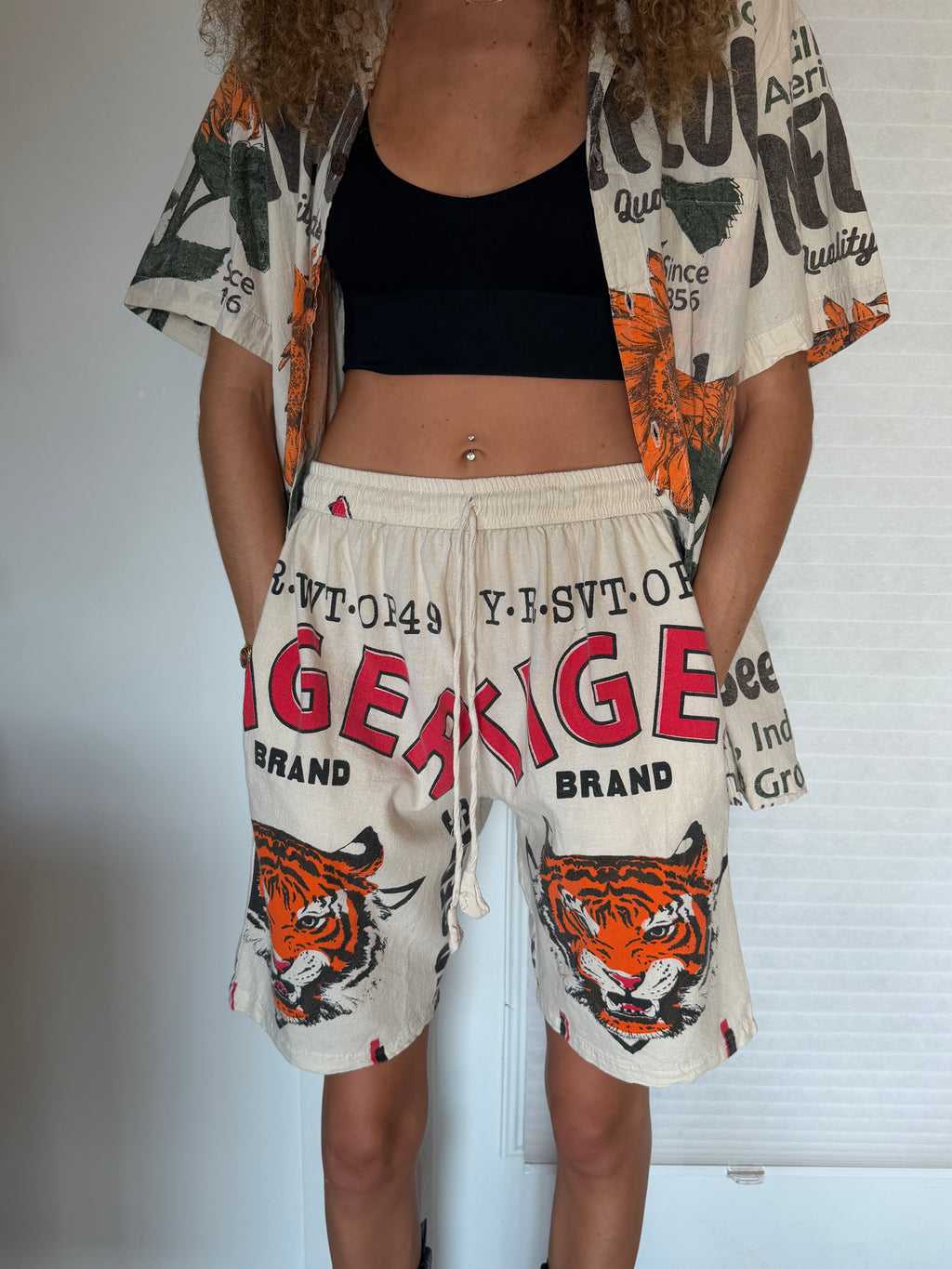 A person wearing cream drawstring shorts with a bold red 'TIGER LIGH' graphic, black text, and two large orange tiger faces on the front. The shorts also feature small red and black flag-like accents.
