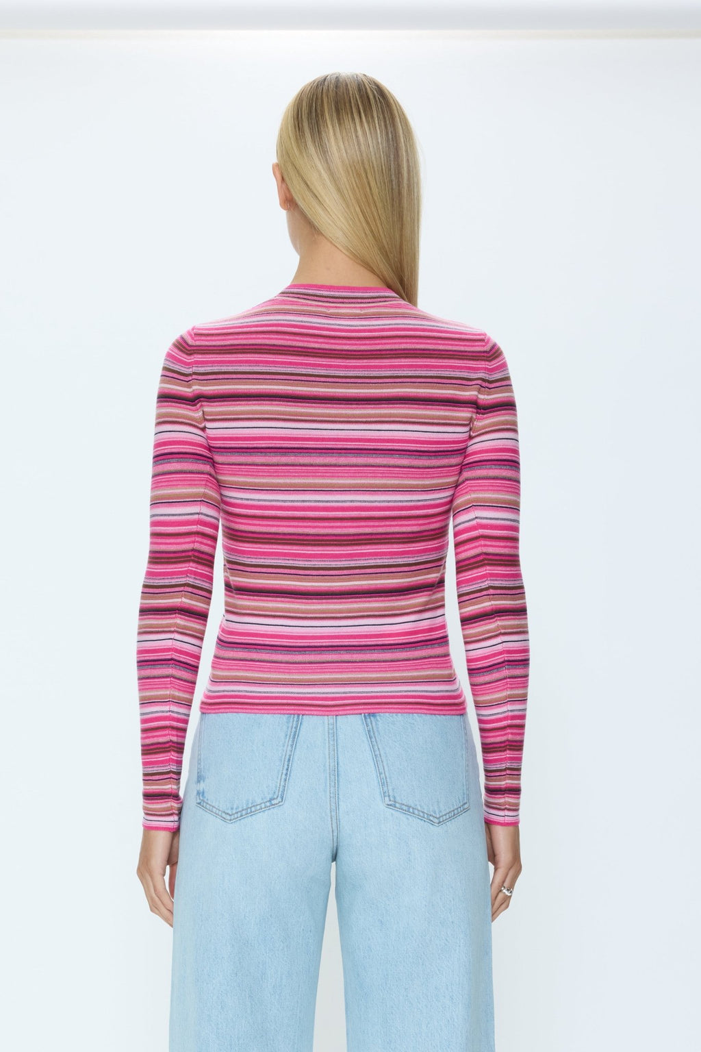 Woman wearing a pink and purple striped sweater with light blue jeans on a white background