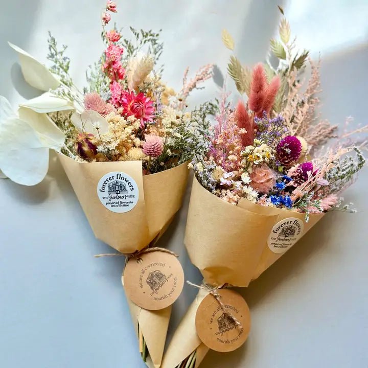 Bouquet of dried flowers wrapped in brown paper with a visible brand label, held by a person against a light background.
