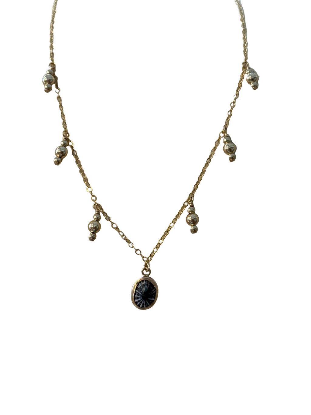 Delicate gold necklace with a black pendant on a beige surface