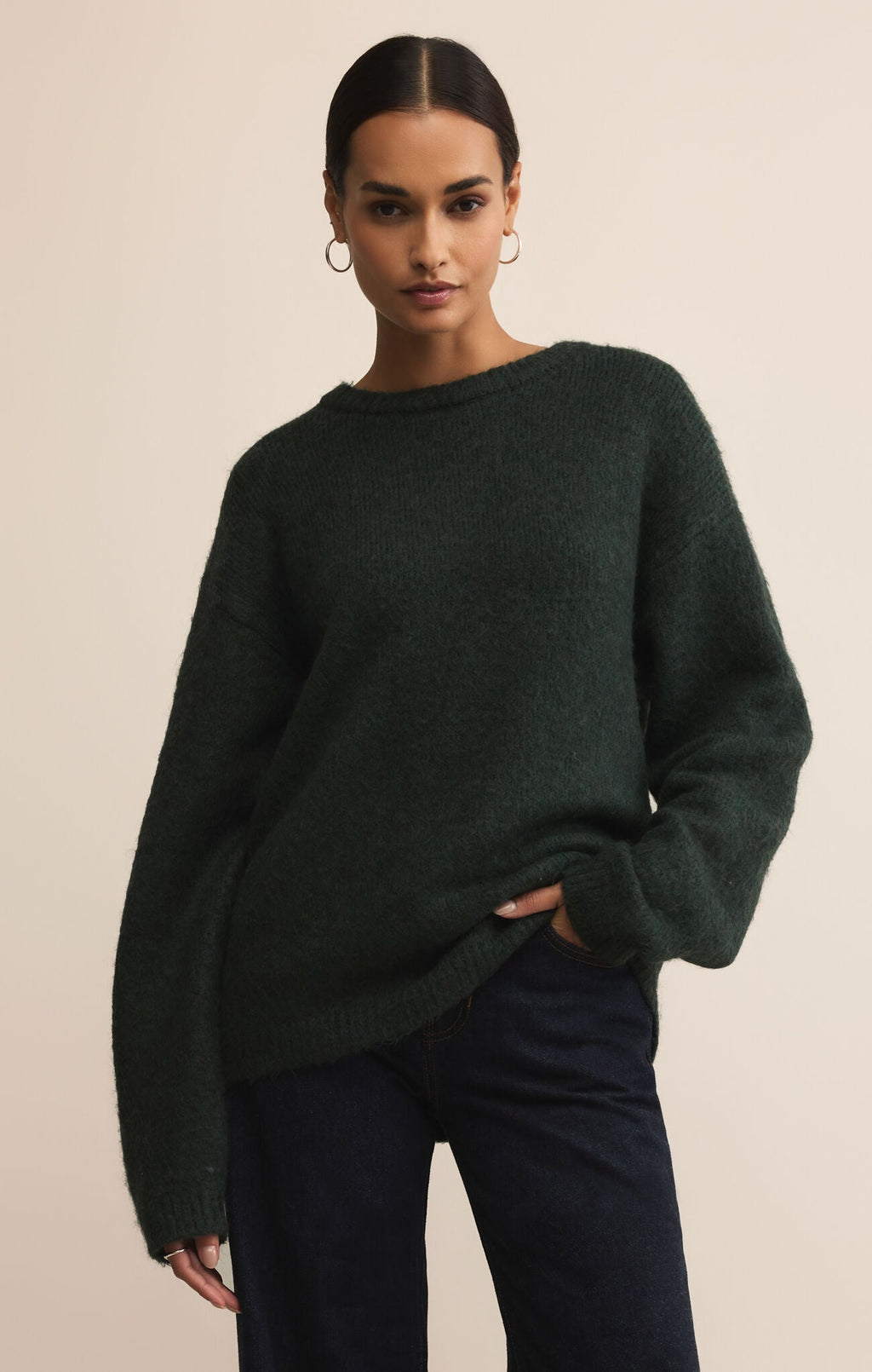 Woman wearing a dark green sweater and dark pants against a beige background