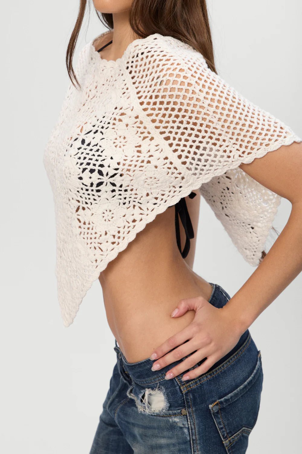 Woman wearing a white crochet top and blue jeans on a plain background